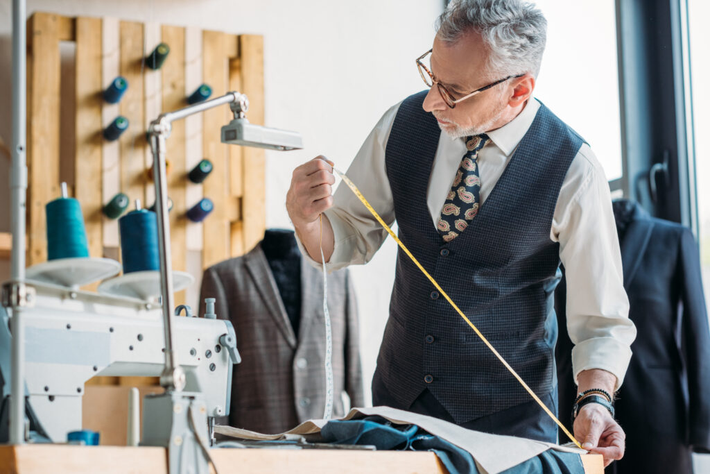 grey hair tailor measuring cloth with tape measure at sewing workshop