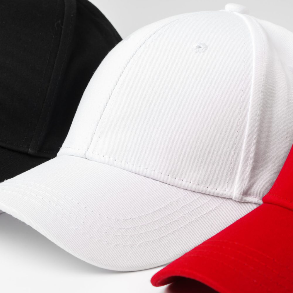 A selection of four baseball caps is neatly arranged in a row, showcasing the colors red, white, and black.